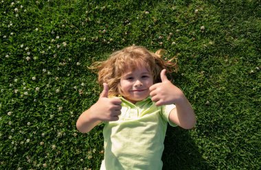Çimenlerin üzerinde yatan çocuk. Başparmağı olan çocuklar, doğa parkında küçük çocuk portresi.