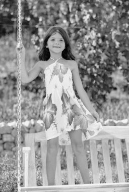 Küçük kız güneşli bir yaz gününde sallanıyor. Salıncakta sallanan çocuk. Güneşli bir yaz gününde parkta sallanan bir çocuk. Yazın açık hava aktivitesi. Oynayan çocuk