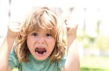 Öfkeli ifadeli bir çocuk. Öfkeli, küçük, öfkeli çocuk, öfkeli çocuk. Öfkeli çocuklar yüzlerini kapatıyorlar. Öfkeli portresi olan nefret dolu bir çocuk. Çocuk yumruğuyla dövüşüyor.