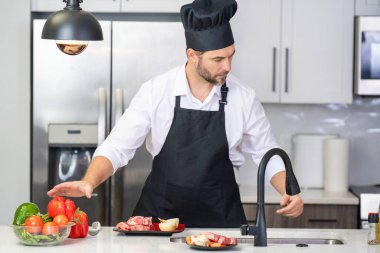 Şef olgun aşçı mutfakta önlük giyer. Yakışıklı adam mutfakta yemek hazırlıyor. Lezzetli yemek pişiren adam. Mutfakta et ve sebzeli bir adam. Mutfakta önlüklü sıradan bir adamın portresi.