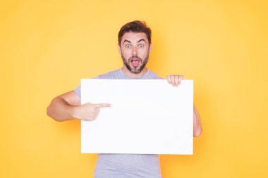 Boş afişi olan şaşırmış bir adam stüdyo arka planında izole edilmiş. Boş posteri olan çekici bir adamın portresi. Poster gösteren, tabela üzerinde parmak gösteren bir adam. Pano veya afiş konsepti