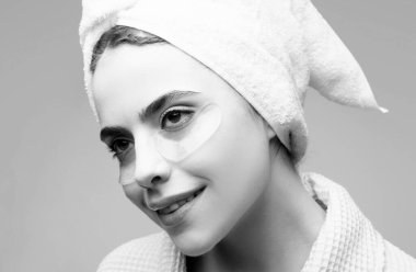 Woman applying eye patches. Close up portrait girl with towel on head. Portrait of beauty woman with eye patches showing an effect of perfect skin. Brunette spa girl clipart
