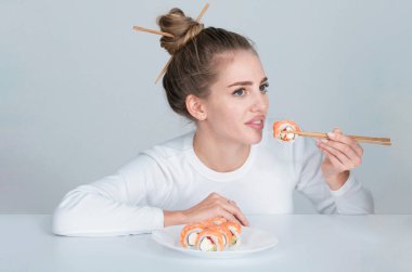 Japon kadın suşi stili. Japon suşi seti yiyorum. Yemek çubuğuyla suşi yiyen güzel genç bir kadın, beyazın üzerinde izole edilmiş. Çubuklu suşi. Sağlıklı Japon yemekleri