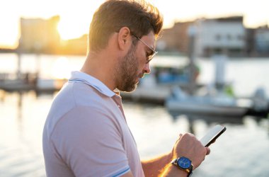 Polo giymiş şık bir adam telefonda konuşuyor. Moda erkeği sokakta poz veriyor. İş telefonu konuşması. Şehir tarzı. Genç adam şehirde yürüyor.