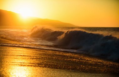 Dalgalar sıçrıyor. Altın gökyüzü ve okyanus suyu. Deniz dalgaları arka planı. Günbatımında deniz manzarası ve tropikal plaj ya da tatil ve tatil için gün doğumu. Okyanus suyu ve kumsalda kum