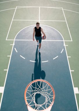 Basketbolcu, tişörtlü ve şortlu sporcu, basketbol topunu şehir arka planında tutuyor. Spor motivasyonu kavramı