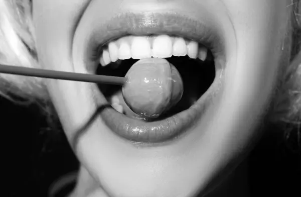 Sensual red lips with candy for print. Red lollipop in the mouth in art design. Glossy womans lips licking sucking lollipop. Sensual sexy mouth with candy concept enjoyment beautiful female lips