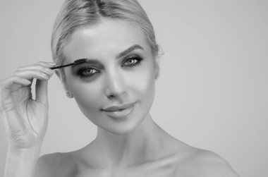Beautiful woman applies brow gel with brows brush to her eyebrow. Studio portrait of young woman doing her eyebrow natural make up. Eyebrows make up concept clipart