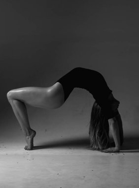 Gri stüdyo arka planında poz veren güzel bir kadın dansçı. Esnek seksi kadın. Şehvetli kız zayıf vücudunu esnetiyor. Zarif bir bayan jimnastikçi mükemmel biçimli vücuduyla poz veriyor. Fıçıları geriyorum