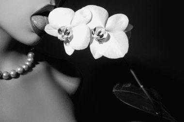 Seksi kadın dili çiçeği yalıyor. Orkide ve kadın dudakları. Şehvetli kadının ağzında orkide çiçeği