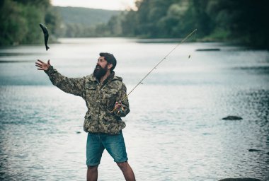 Genç sakallı adam gölde ya da nehirde balık tutuyor. Sinek avı