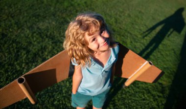 Yaz parkında oyuncak uçak kanatlarıyla oynayan tatlı bir çocuk. Yenilik teknolojisi ve başarı konsepti. Çocuk pilot parkta çimlerde eğleniyor.