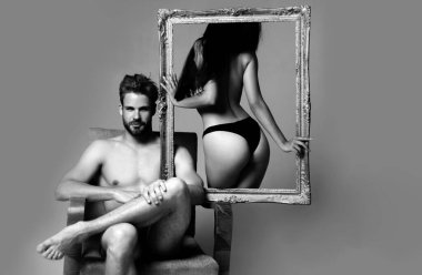 Elinde çerçeve tutan genç bir kadının portresi. Bir çift. Siyah iç çamaşırlı mükemmel vücutlu şehvetli kadın kaslı adamın yanında duruyor. Aile portresi için poz ver. Sevgililer Günü. Romantik ve aşk