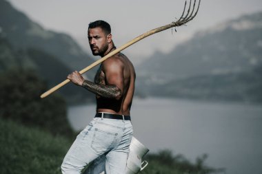 Taşralı seksi adam. Taşrada saman tarlasında kaslı gövdeli bir çiftçi. Kırsal İsviçre, kırsal Alpler. İsviçre 'nin kırsal kesimlerinde erkek çiftçi çim çiftliği, saman tarlası