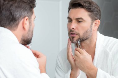 Erkek saç stili, saç kesimi. Elinde makas olan adam. Erkek saç bakımı, güzellik berberi konsepti. Makasla sakallı bir adamın portresi. Tıraşsız adam saçını makasla kesti. Sakal şekillendirme ve makasla kes