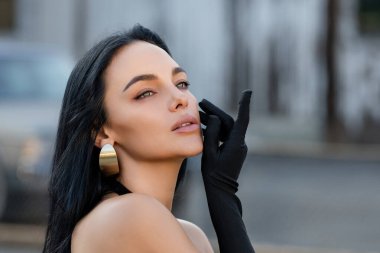 Sokakta poz veren güzel esmer kadın portresi. Moda dünyasından genç ve güzel bir kızın yakın plan kadın portresi, yaz sokak modası. Şık bir açık hava kadınının yüksek moda yakın plan portresi