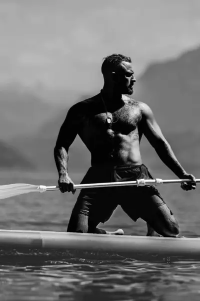 stock image Strong muscular man with paddle board. Man paddling on paddleboard. Muscular strong Hispanic man on sup board paddle surfing. SUP surfing in summer vacation in Alps lake in Switzerland