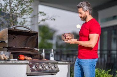 Barbekü. Adam dışarıda barbekü ızgarası hazırlıyor. Adam arka bahçede ızgarada lezzetli yemekler pişiriyor. Şef barbeküde yemek hazırlıyor. Milenyum adamı ızgarada et pişiriyor. Mangal. Izgara yemek.