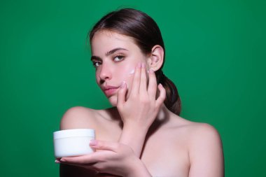 Skin care. Woman applying face cream, studio portrait. Beautiful model with moisturizing cream anti age cream on perfect soft skin. Beauty cosmetic product industry