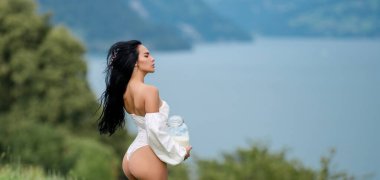 Süt konsepti. Açık havada iç çamaşırlı seksi bir kadın. İsviçre Alplerinde sütlü seksi esmer kadın. Alp köylü kızı. Alp kırsalına karşı bir şişe çiğ süt. Alplerde sütlü seksi kadın