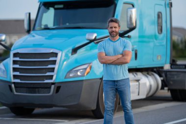 Kamyonun yanında erkek sürücü var. Kamyon şoförü. Milenyum kamyoncusu. Kamyon sahibi. Ulaşım endüstrisi araçları. Kamyonun önünde poz veren yakışıklı bir adam.