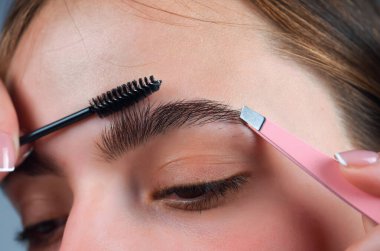 Kaşlar şekilli. Kadının kaş makyajı yaptırmasına yakın çekim. Makro kaşına fırçayla kozmetik uyguluyordu. Mükemmel bir kaş şekli, kahverengi göz farı ve uzun kirpikleri. Şekli kaşlar