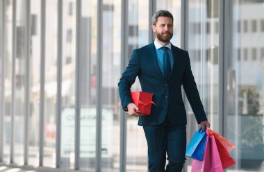 Alışveriş torbaları tutan ve alışveriş mağazasında yürüyen bir iş adamı. Alışveriş ve ödeme. Alışverişkolik alışveriş kavramı