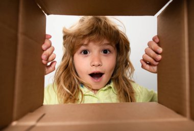 Çocuklar için karton kutuları açıyorum. Mutlu küçük çocuk hediyesini açıyor ve karton kutunun içine bakıyor.