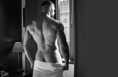 Oturma odasında pencere perdelerinde seksi çıplak genç adam. Çıplak erkek vücudu. Seksi manken. Seksi vücutlu genç kaslı adam. Çıplak göğüs. Kaslı erkek gövdesi, çıplak omuzlar.