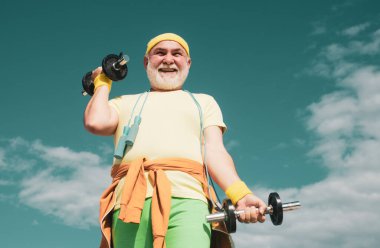 Lifting dumbbells. Healthy lifestyle concept. Senior man lifting weights. Happy Senior sportman exercising with lifting dumbbell on blue sky background. Isolated, copy space