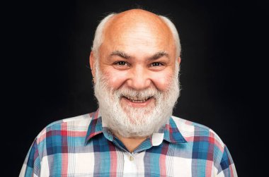 Mutlu, olgun bir adam gülümsüyor. Siyah stüdyo geçmişinde gri sakallı, kel, olgun yaşlı bir adamın portresi.