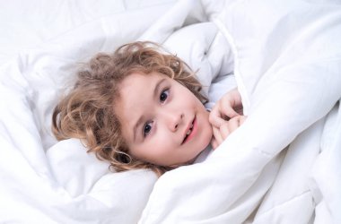 Yatakta uyanan sevimli çocuk, uyku zamanı, çocukluk ve büyüyen çocuk konsepti, kapalı mekan portresi