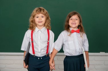 Okul üniformalı arkadaş canlısı sınıf arkadaşları dersteler. Okul çocukları, arkadaşlık, okul arkadaşları. Sınıf arkadaşları, genç ilkokul öğrencileri karatahtanın yanında el ele tutuşuyorlar.