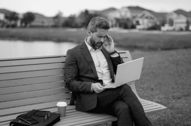 Takım elbiseli yorgun iş adamının bankta oturmasından sıkıldım. Yorgun yönetim kurulu başkanı dizüstü bilgisayarda çalışıyor. Yorgun iş adamları streslidir. Baş ağrısı migreni. Parkta dizüstü bilgisayardan çalışan yorgun serbest çalışan bir adam.