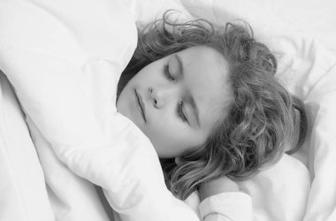 Sakin çocuklar uyur. Küçük çocuk yatakta uyuyor. Yatakta battaniyenin altında yalnız uyuyan tatlı bir çocuk. Çocuk konfor yastığında yatıyor, sevimli küçük çocuk uyuyor, sağlıklı bir uyku çekiyor ya da kestiriyor.