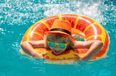 Havuzda yüzen çocuk yüzen yüzükle oynuyor. Güneş gözlüklü sevimli çocuk yaz günü havuzda şişme yüzüklerle yüzer. Çocuk deniz suyunda havuz yüzüğüyle rahatla