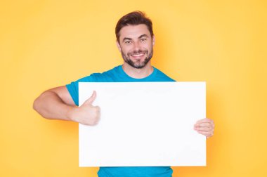 Man holds the white sign, blank card. Placard ready for your product. Sign to your text. Man showing thumbs up and blank sign board over studio background. Empty blank board. Area for advertising