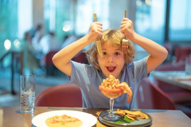 Funny surprised Little boy eating seafood in cafe. Kid eat Food fish gourmet seafood shrimp in restaurant. Adorable little boy at restaurant having breakfast