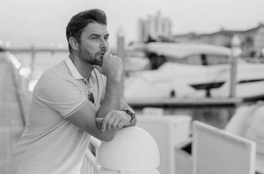 Yatın yanında hayal kuran ve düşünen zengin bir iş adamı. Moda erkeği sokakta poz veriyor. Şehir tarzı. Genç adam şehirde yürüyor. Varlıklı işadamı ofis binasının yanında poz veriyor.