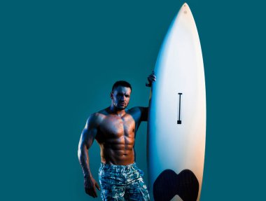 Mavi üzerinde neon sörf tahtası olan kaslı bir adam. Formda sörf yapan bir erkek. Sörf tahtası olan seksi bir sörfçü. Yaz sporu
