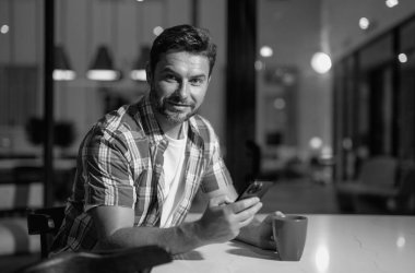 Adam evde telefona bakıyor, mobil uygulamalara bakıyor, haberleri okuyor, sohbet ediyor ya da internetten alışveriş yapıyor, akıllı telefon tutuyor. Oturma odasında rahat giyinmiş, cep telefonuyla konuşan çekici bir adam.