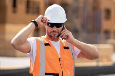 Bir şantiyede inşaat projesinde çalışan şapkalı bir inşaatçı. Çalışanlar telefon kullanıyor, inşaatçılar işe ara veriyor. Cep telefonlu mimar