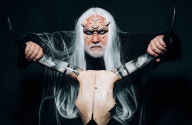 Şeytan korku konsepti. İki kırmızı boynuz tutan yaşlı bir adam. Beyaz mavi gözlü canavar. Boynuzlu kafalı bir Viking. Ejderha derisi ve gri sakallı bir uzaylı. Kötü vampir adam.