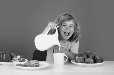 Kahvaltıda süt içen heyecanlı bir çocuk. Çocuk süt içiyor. Süt döken çocuk, izole edilmiş stüdyo portresi