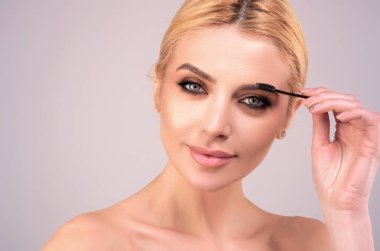 Beautiful woman applies brow gel with brows brush to her eyebrow. Studio portrait of young woman doing her eyebrow natural make up. Eyebrows make up concept clipart