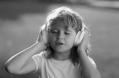 Şarkı söyleyen çocuklar. Hayal gören çocuk yeşil çim arka planda kulaklıkla müzik dinlemeyi seviyor. Kulaklıklı komik çocuk yaz parkında ya da arka bahçede müzik dinliyor.