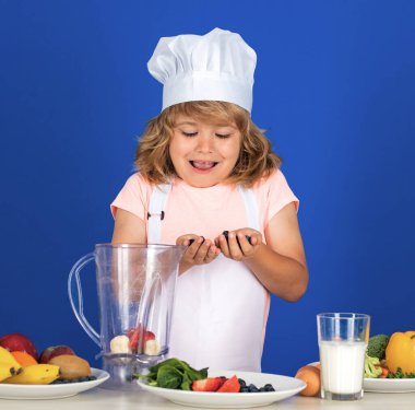 Yemek pişiren çocuklar. Aşçı çocuk sağlıklı yemek için taze sebze yapıyor. Gri arka planda izole edilmiş küçük çocuk portresi. Aşçı çocuk. Yemek pişirme süreci