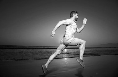 Koşan bir koşucu. Genç adam inanılmaz bir günbatımında denizin sahilinde koşuyor.