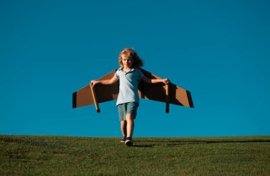 Uçakta uçan çocuk mukavva kanatlardan yapılmış. Rüya, hayal gücü, çocukluk. Seyahat ve yaz tatili konsepti. Genç pilot mavi gökyüzüne karşı fotokopi ile