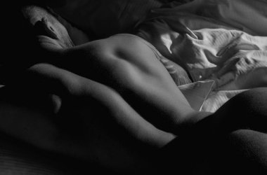 Young sexy man lying on a bed. Handsome young man with naked body, bare torso, undressed. Muscular young man laying on bed with naked muscular body. Sexy young male model